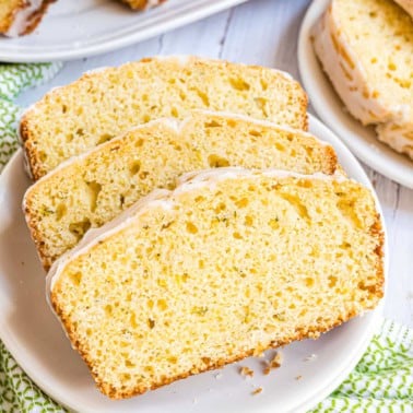 Three slices of glazed lemon zucchini bread on a white plate, showcasing a moist and airy texture.