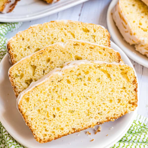Three slices of glazed lemon zucchini bread on a white plate, showcasing a moist and airy texture.