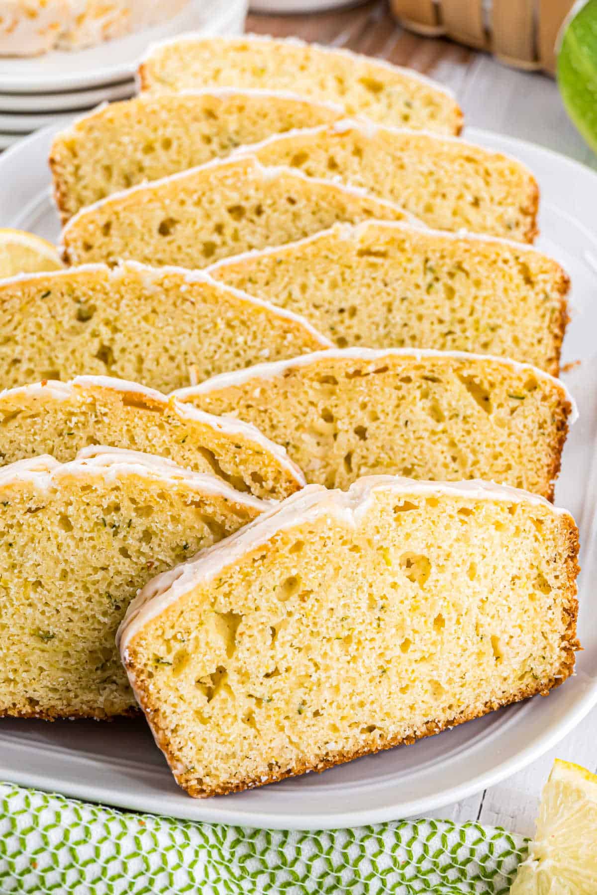 Slices of glazed lemon zucchini bread loaf cake arranged neatly on a white plate.