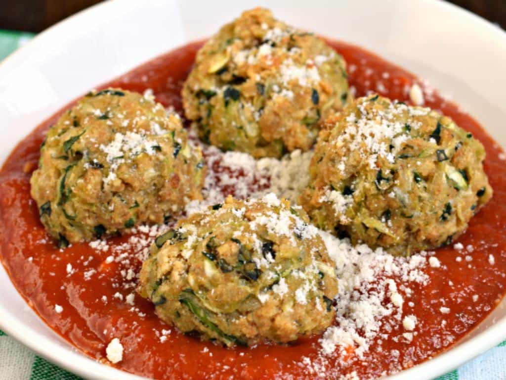 Four zucchini meatballs in a dish with marinara sauce.