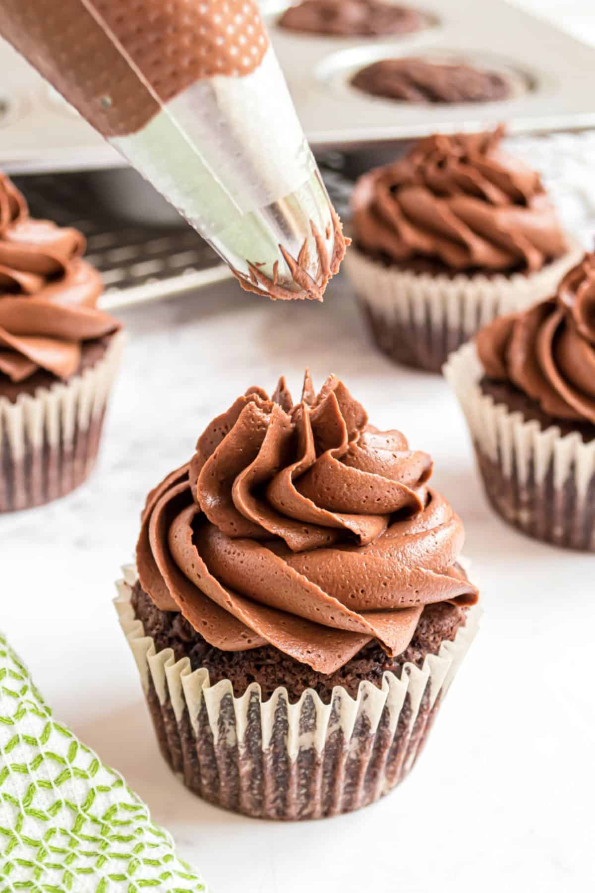 Chocolate frosting being piped onto a chocolate cupcake.