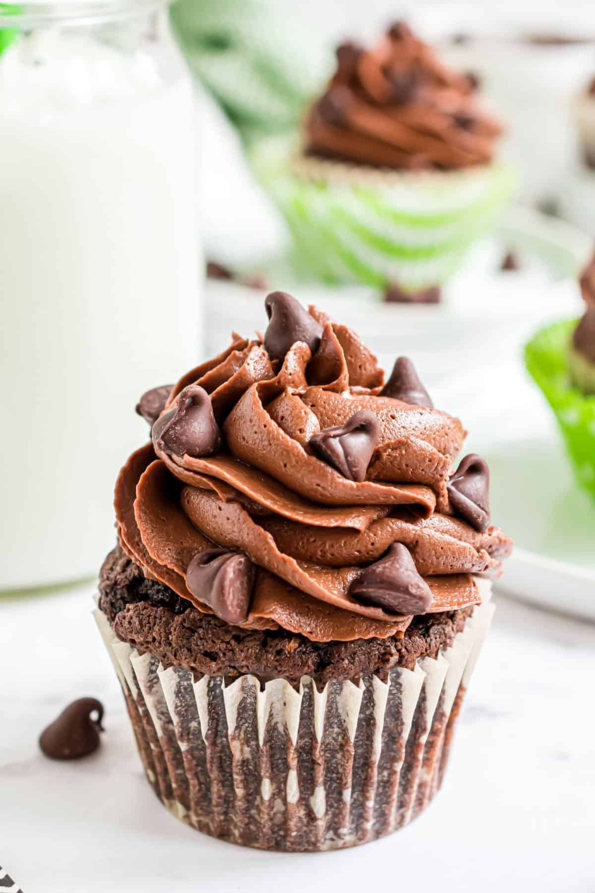 Chocolate cupcake in a white liner topped with chocolate frosting and chocolate chips.