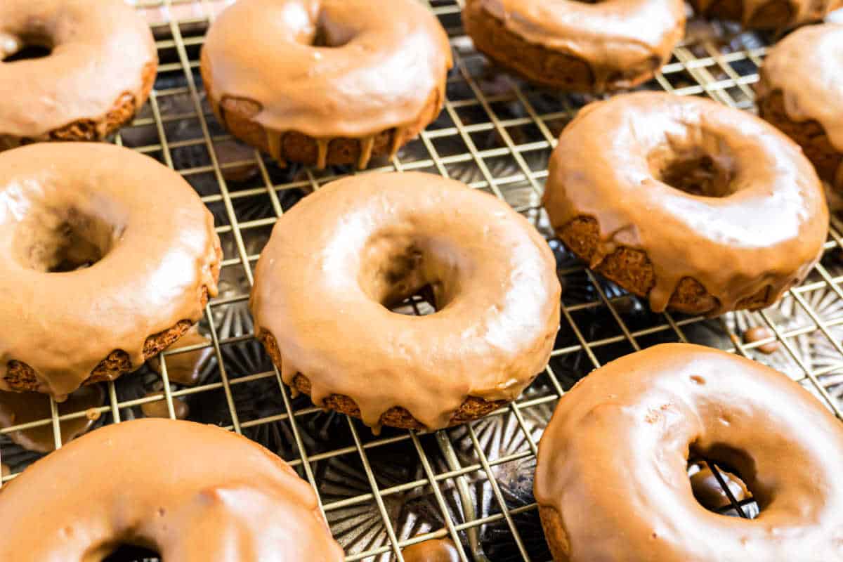 Maple glazed pumpkin donuts cooling on a wire rack, with icing gently dripping down the sides.