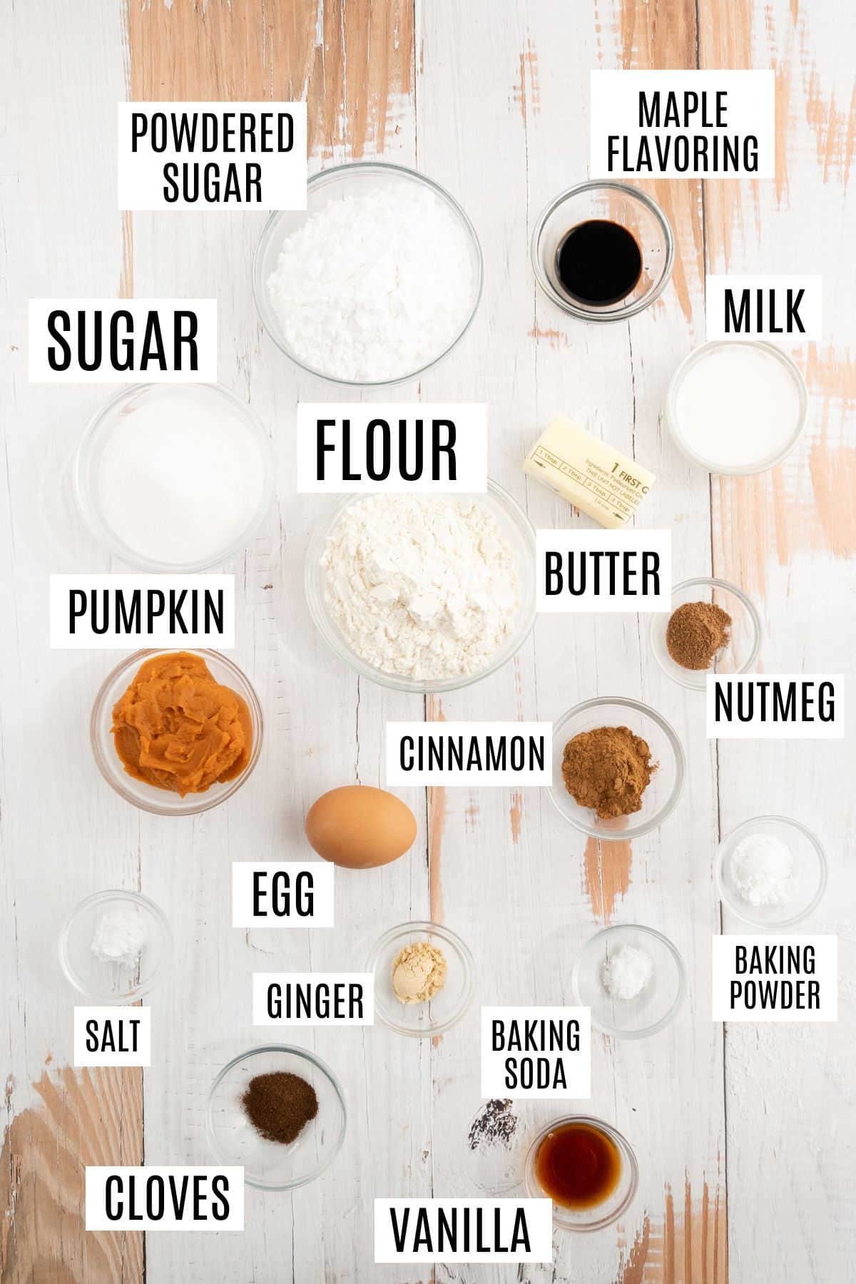 Baking ingredients labeled on a white surface, including flour, sugar, pumpkin, spices, egg, butter, milk, and vanilla—everything you need to make delicious maple glazed pumpkin donuts.