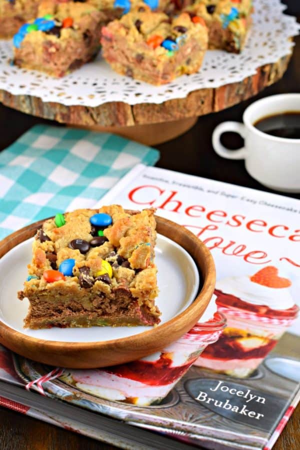 These Monster Cookie Cheesecake Bars are two layers of cookie dough packed with peanut butter and M&M'S candy and filled with a creamy chocolate cheesecake filling! #cookiedough #cheesecake #dessert