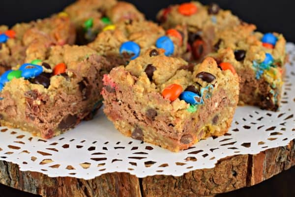 These Monster Cookie Cheesecake Bars are two layers of cookie dough packed with peanut butter and M&M'S candy and filled with a creamy chocolate cheesecake filling! #cookiedough #cheesecake #dessert