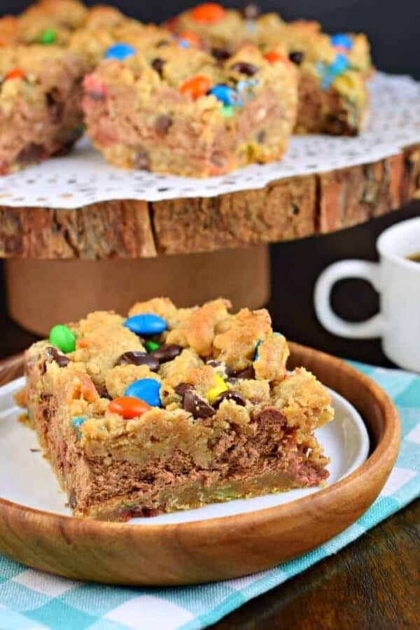 These Monster Cookie Cheesecake Bars are two layers of cookie dough packed with peanut butter and M&M'S candy and filled with a creamy chocolate cheesecake filling! #cookiedough #cheesecake #dessert