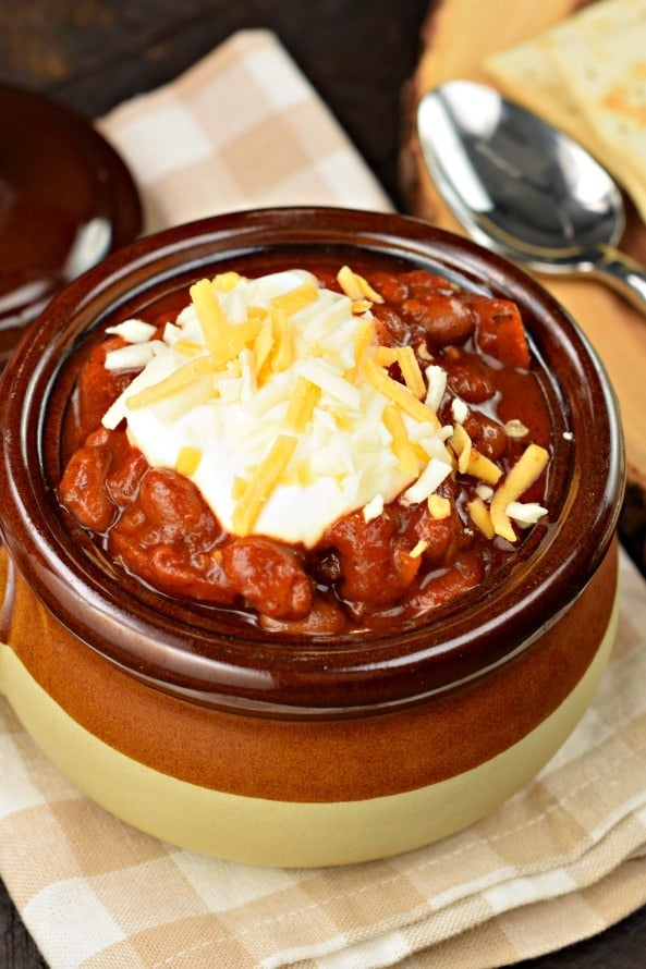 Thick pumpkin chili in a brown stoneware soup bowl with sour cream and shredded cheese topping.