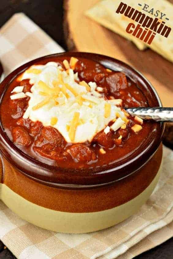 Pumpkin chili in a stoneware crock topped with sour cream and cheese.
