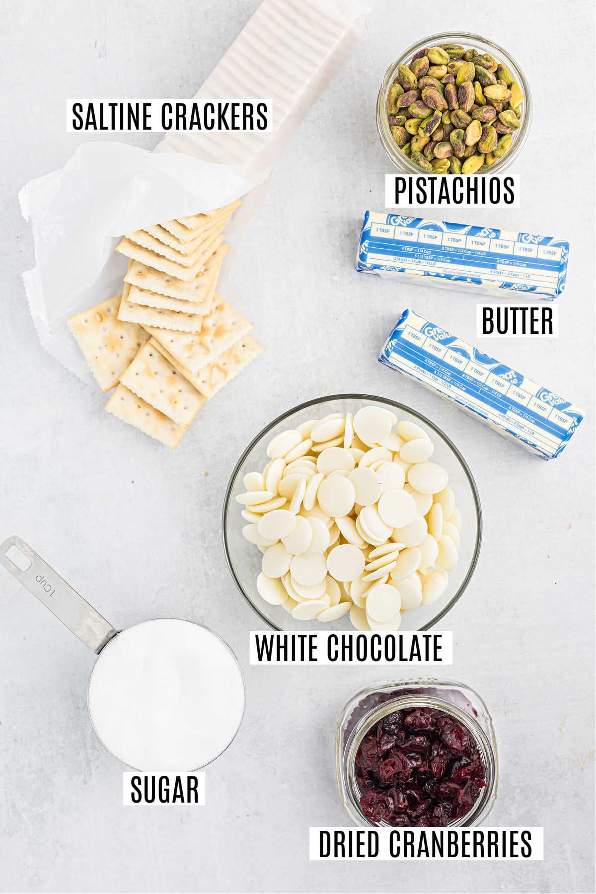 Saltine crackers, pistachios, butter, white chocolate, sugar, and dried cranberries come together to create a tempting cranberry pistachio saltine toffee arranged on a white surface.