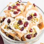 A bowl of cranberry pistachio saltine toffee topped with white icing, dried cranberries, and chopped pistachios.