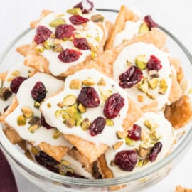 A bowl of cranberry pistachio saltine toffee topped with white icing, dried cranberries, and chopped pistachios.