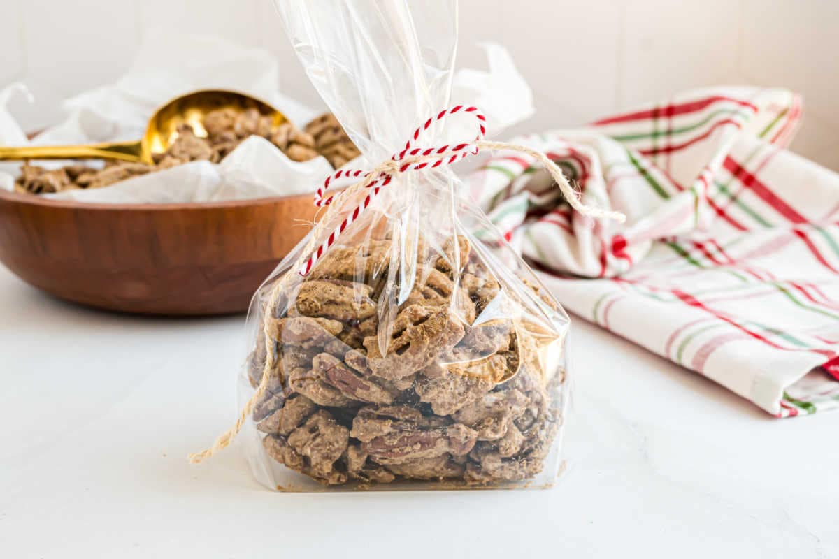 A clear bag of Maple Brown Sugar Pecans tied with red string, with a bowl and plaid cloth in the background.