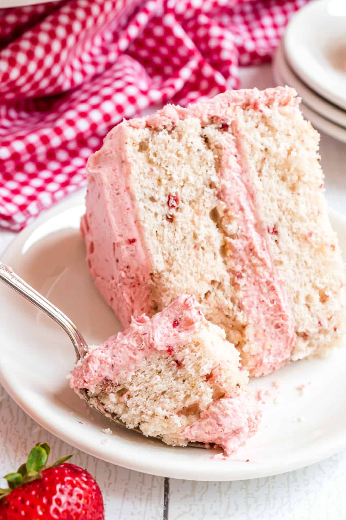 Slice of strawberry cake with a fork taking a bite.