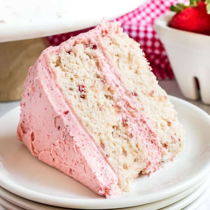 Slice of strawberry layer cake with strawberry frosting on a white plate.