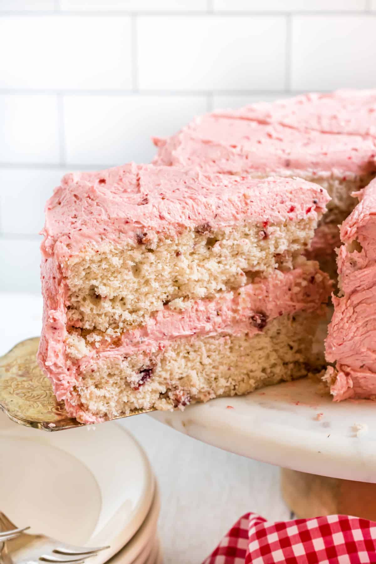 Strawberry layer cake on a cake platter with one slice being removed.