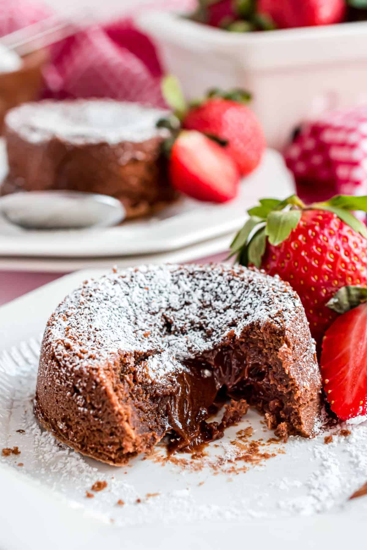 Individual sized chocolate lava cake with gooey center on a white plate with fresh strawberries.