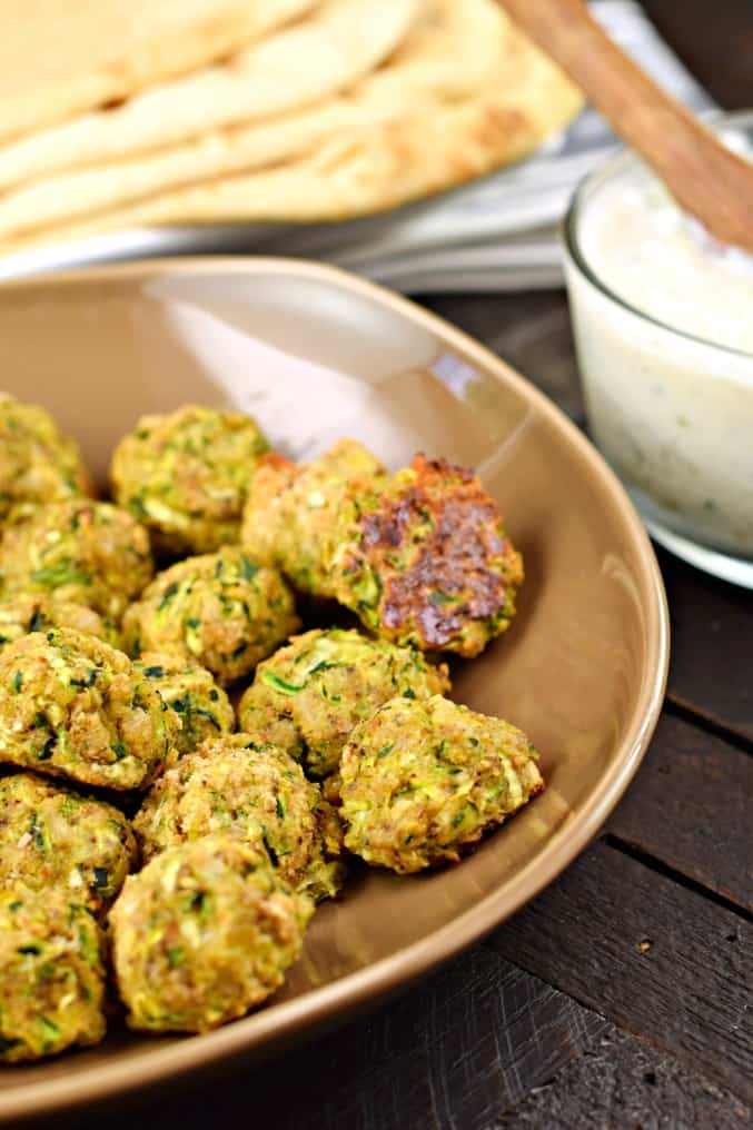 Brown bowl with zucchini meatballs and a side of tzatziki sauce.