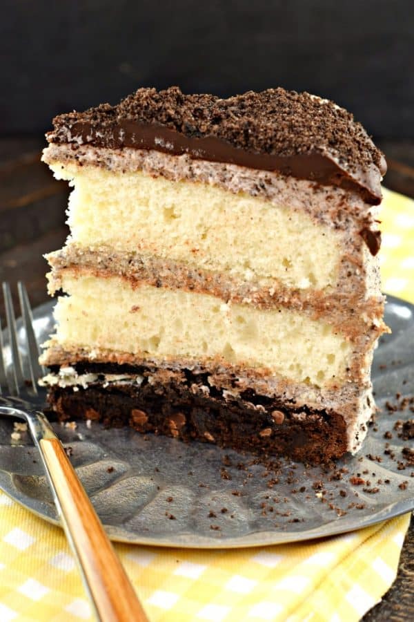 Slice of cake with a brownie bottom, white cake, oreo frosting, and chocolate ganache.