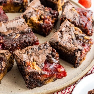 Chocolate brownies with a gooey strawberry jam filling, inspired by classic peanut butter jelly brownies, served on a plate.