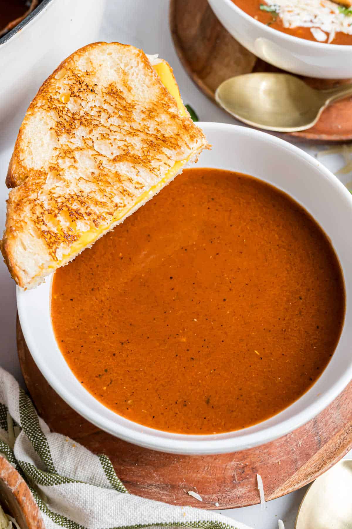 Bowl of roasted tomato soup with a grilled cheese sandwich resting on the edge of the bowl.