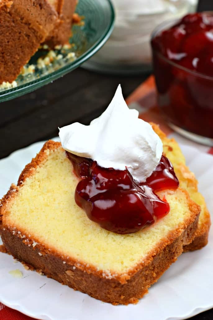 Two slices of pound cake on a white dessert plate, topped with strawberry pie filling and whipped cream.