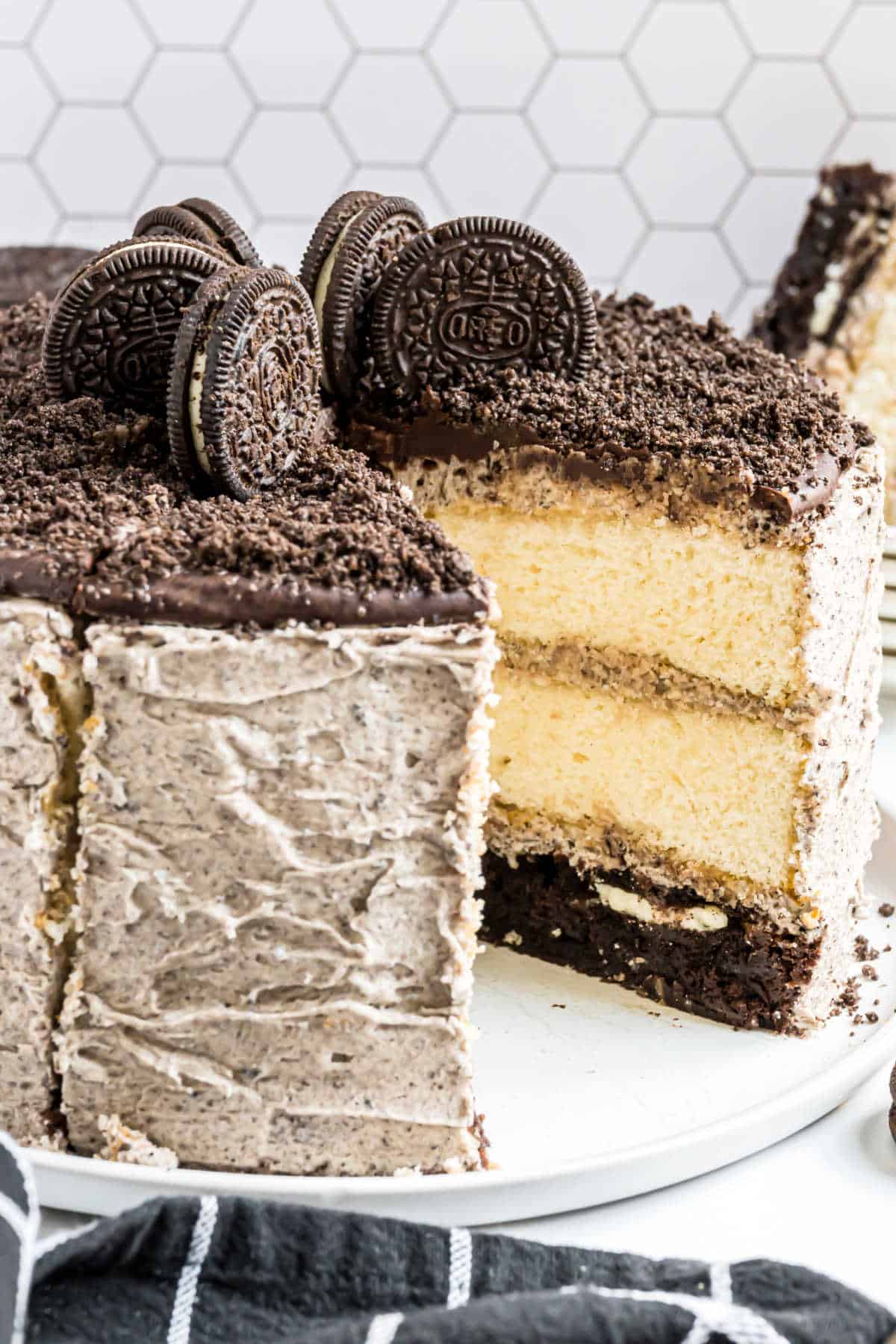A layered oreo brownie cake topped with whole Oreo cookies and Oreo crumbs, with one slice cut out.