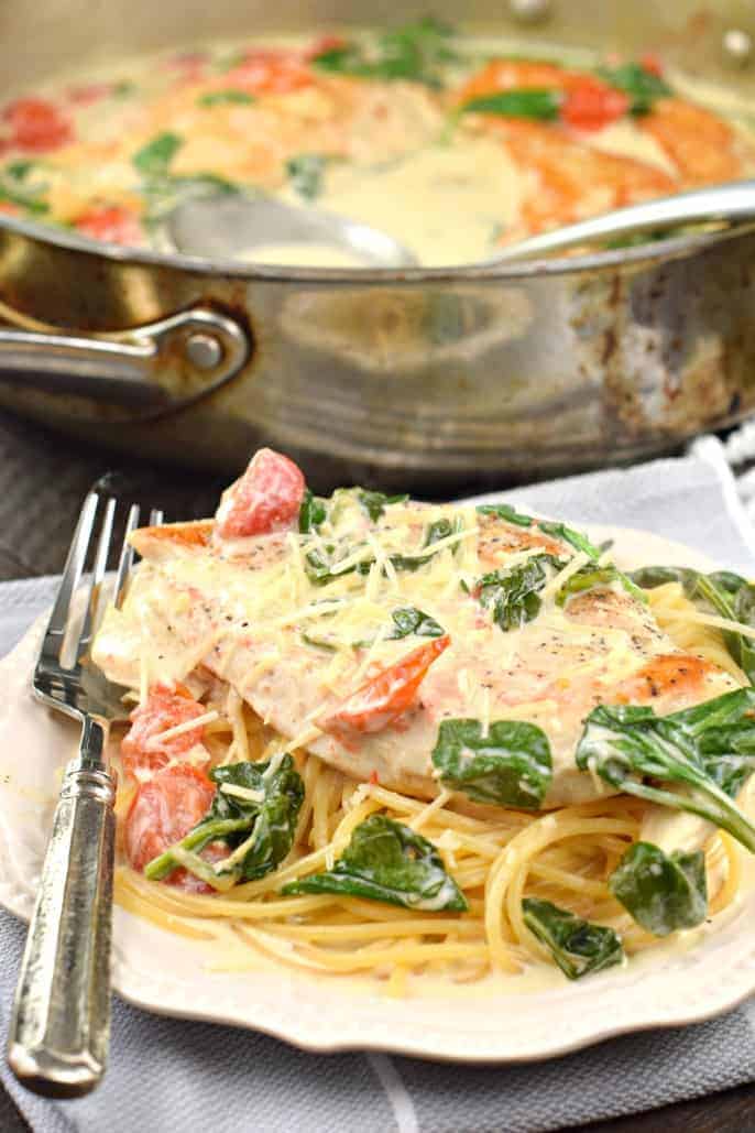Chicken served over a mound of pasta with spinach and tomatoes.