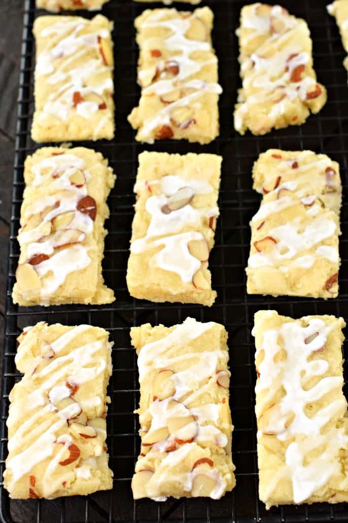 Almond bars topped with vanilla glaze cut into rectangles on a wire rack to cool.