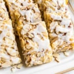 Rectangular almond pastry bars topped with sliced almonds and white icing, arranged on a white plate—an irresistible treat inspired by a classic almond bars recipe.