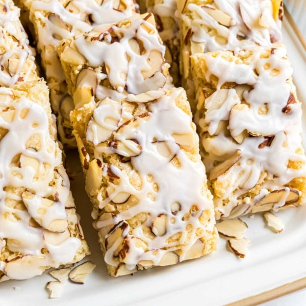 Rectangular almond pastry bars topped with sliced almonds and white icing, arranged on a white plate—an irresistible treat inspired by a classic almond bars recipe.