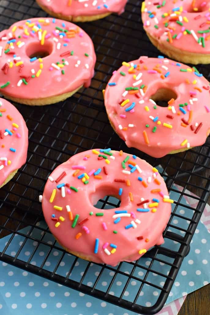 These Cherry Frosted Donuts have a tender, moist cake-like texture with a dreamy cherry frosting! Perfect for holidays, Valentine's Day, or general breakfast enjoyment. CHerry donuts with sprinkles on a wire rack.