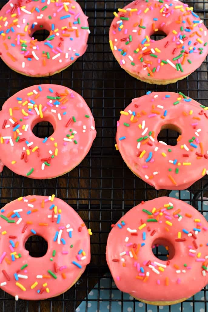 These Cherry Frosted Donuts have a tender, moist cake-like texture with a dreamy cherry frosting! Perfect for holidays, Valentine's Day, or general breakfast enjoyment. Six cherry frosted donuts on a black wire rack.