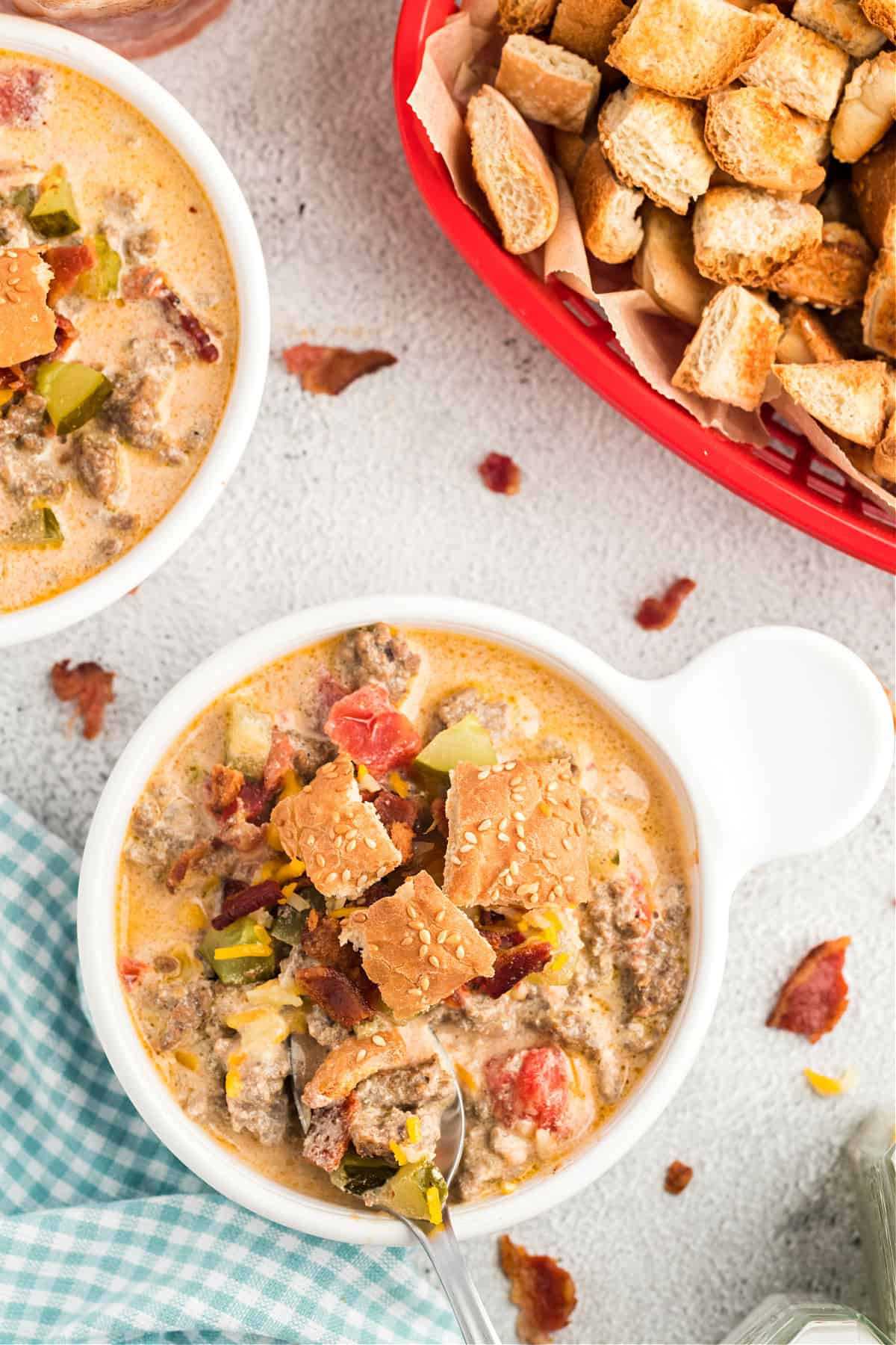 Bowl of cheeseburger soup topped with crispy bacon and hamburger bun croutons.