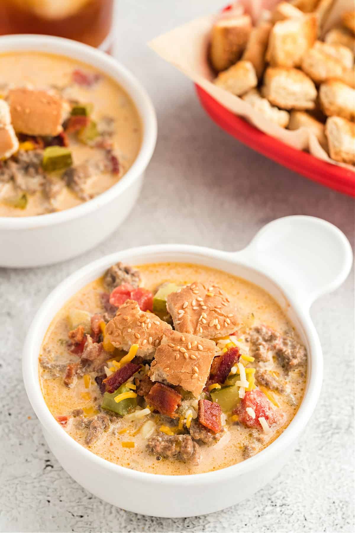 Two bowls of cheeseburger soup topped with hamburger bun croutons.