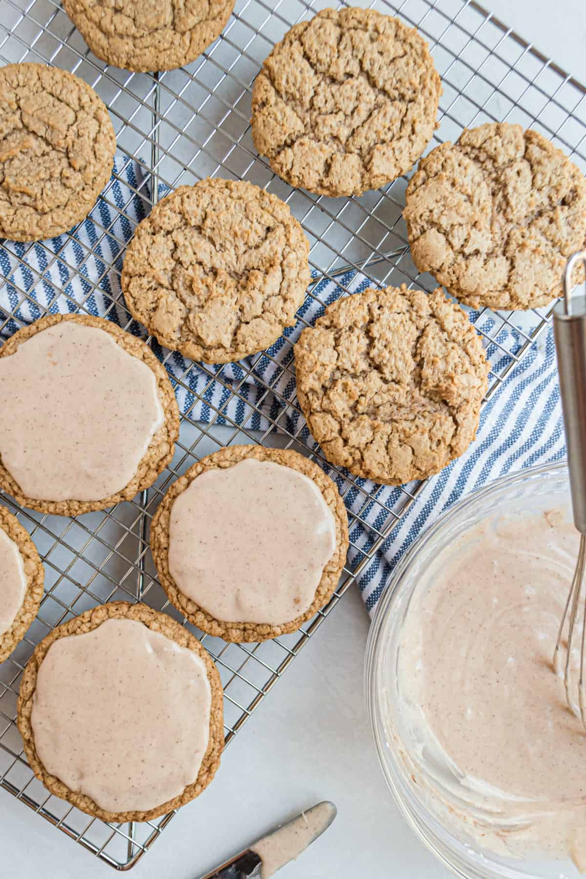 Glaze for iced oatmeal cookies in a bowl being spread on cookies.