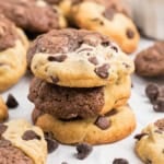 A stack of marbled Brookie Cookies, where the rich layers of brownie and chocolate chip cookies intertwine, with scattered chocolate chips on a pristine white surface.