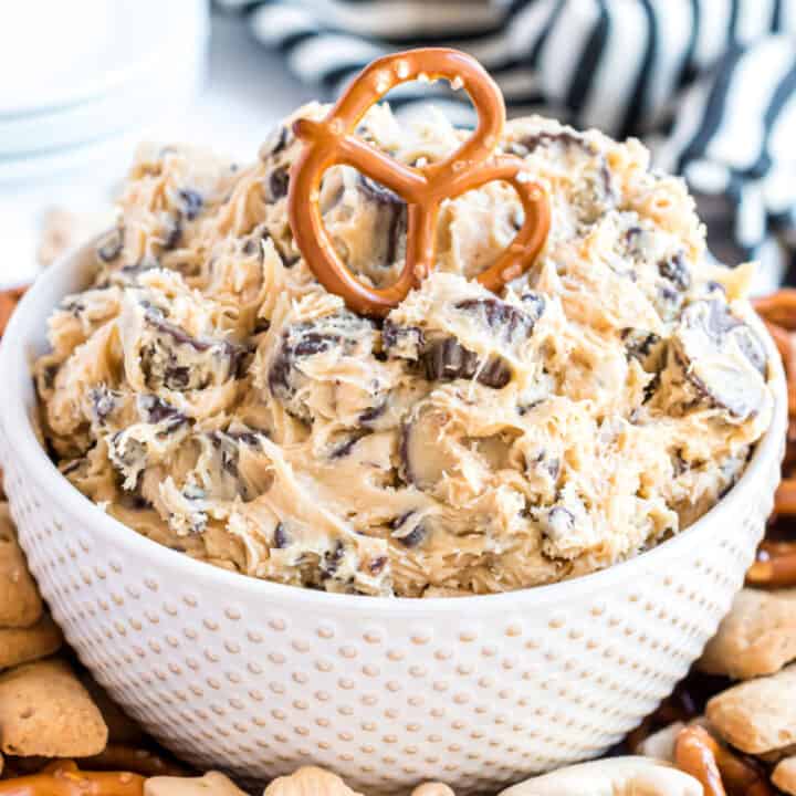 Peanut butter cookie dough dip in a white bowl with a pretzel dipper on top.