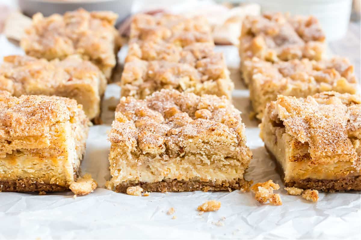 Snickerdoodle cheesecake bars cut into squares on parchment paper.