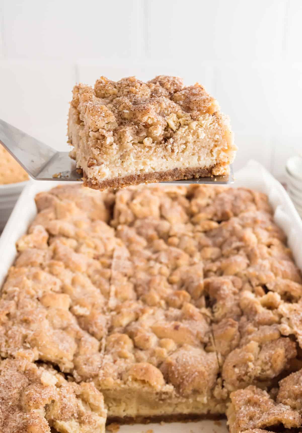 Snickerdoodle cheesecake bar being lifted out of pan with spatula.