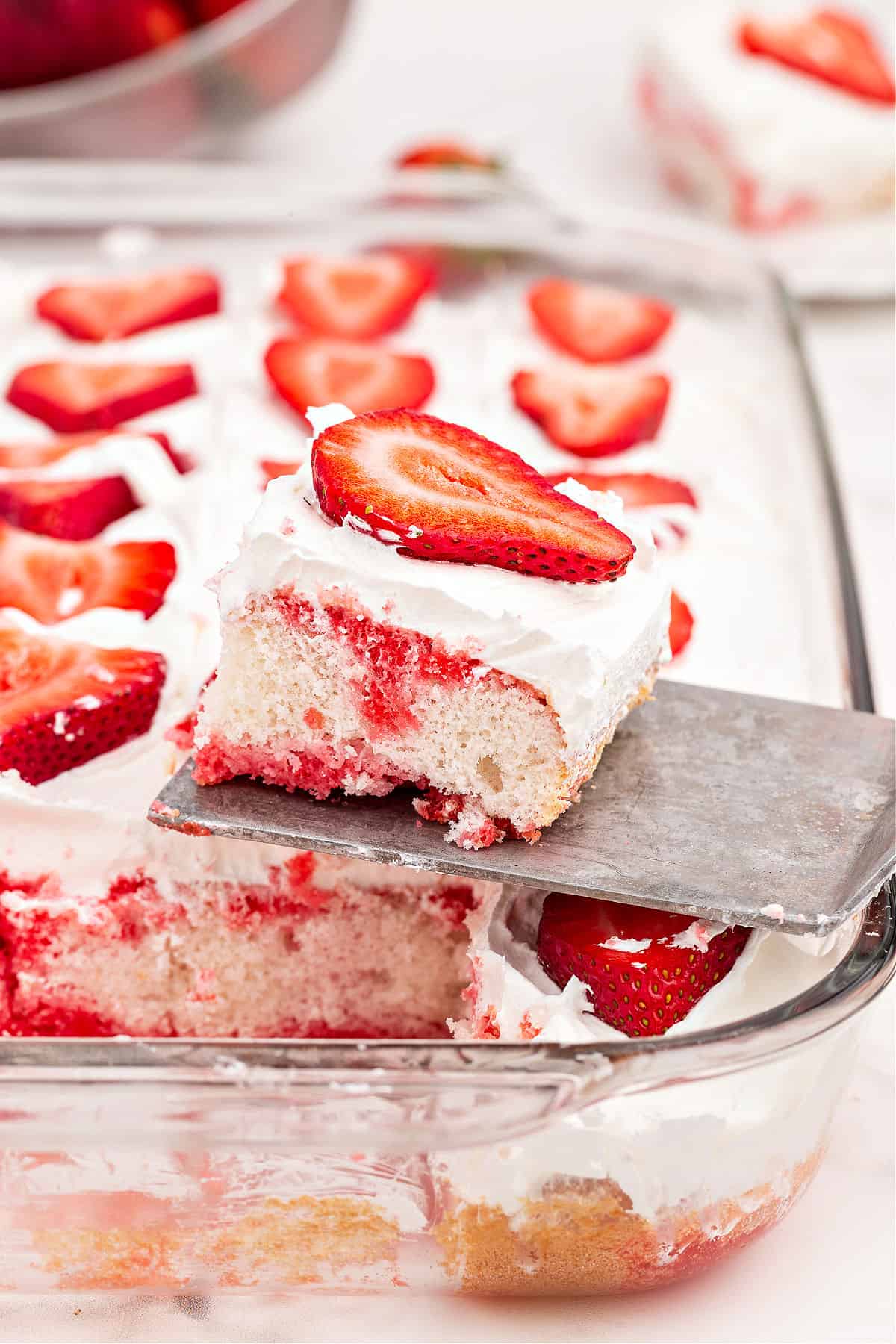 Slice of jello poke cake on spatula being lifted out of pan.