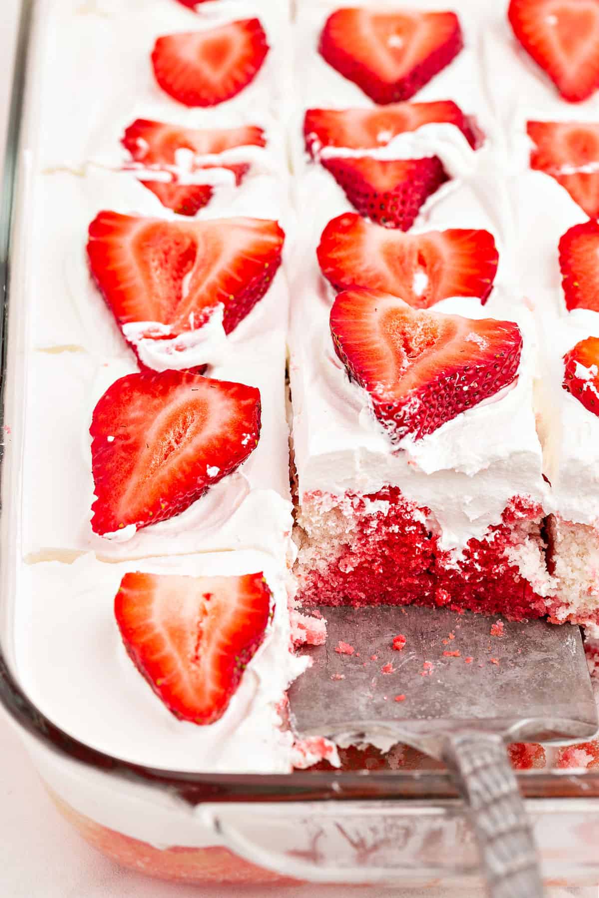 Clear glass baking dish with strawberry poke cake and one slice removed.