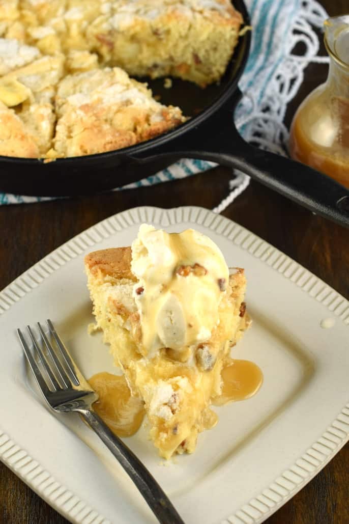 Slice of butter pecan apple cake on a white plate and topped with ice cream.