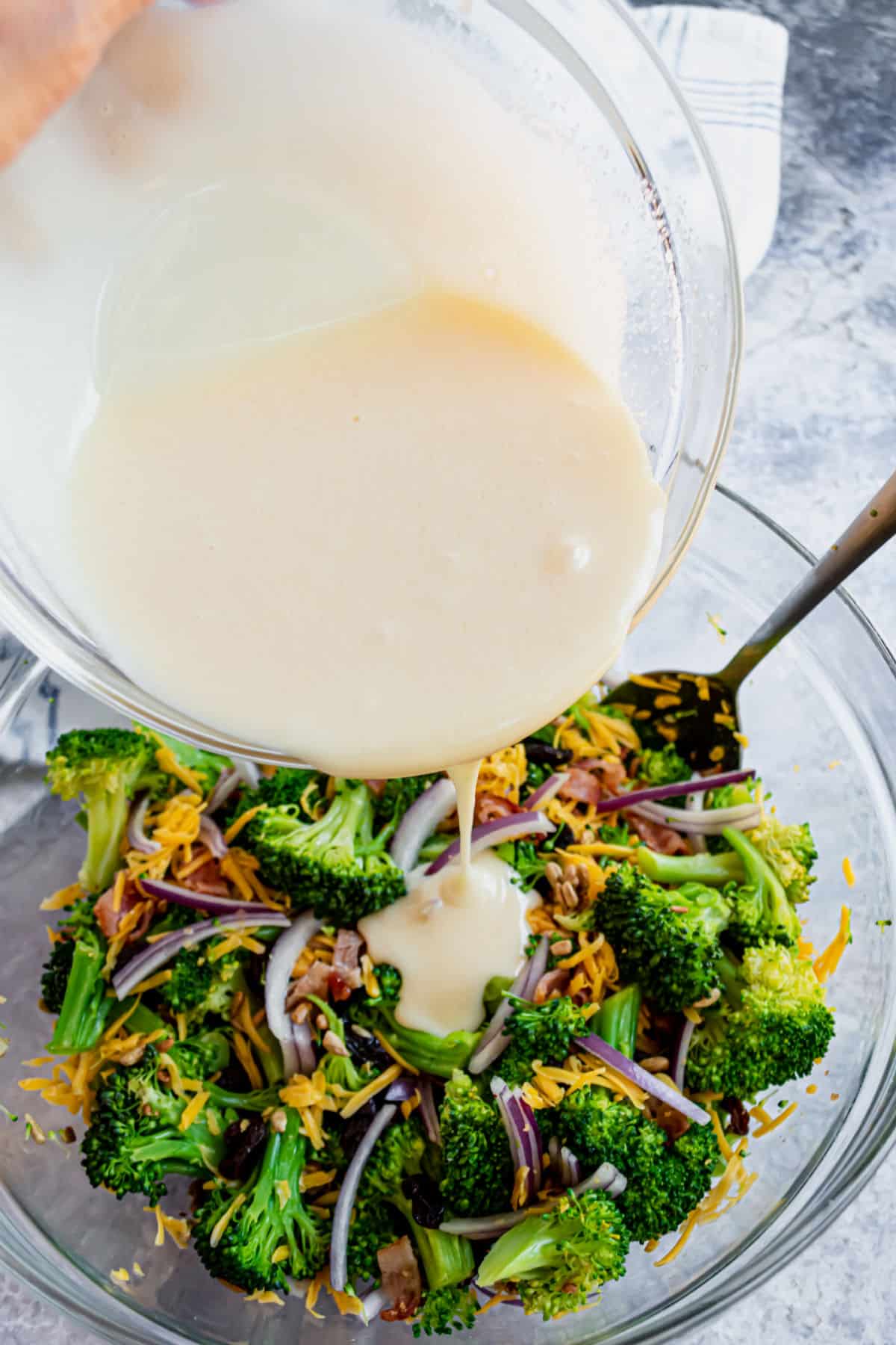 Dressing being poured over broccoli salad.