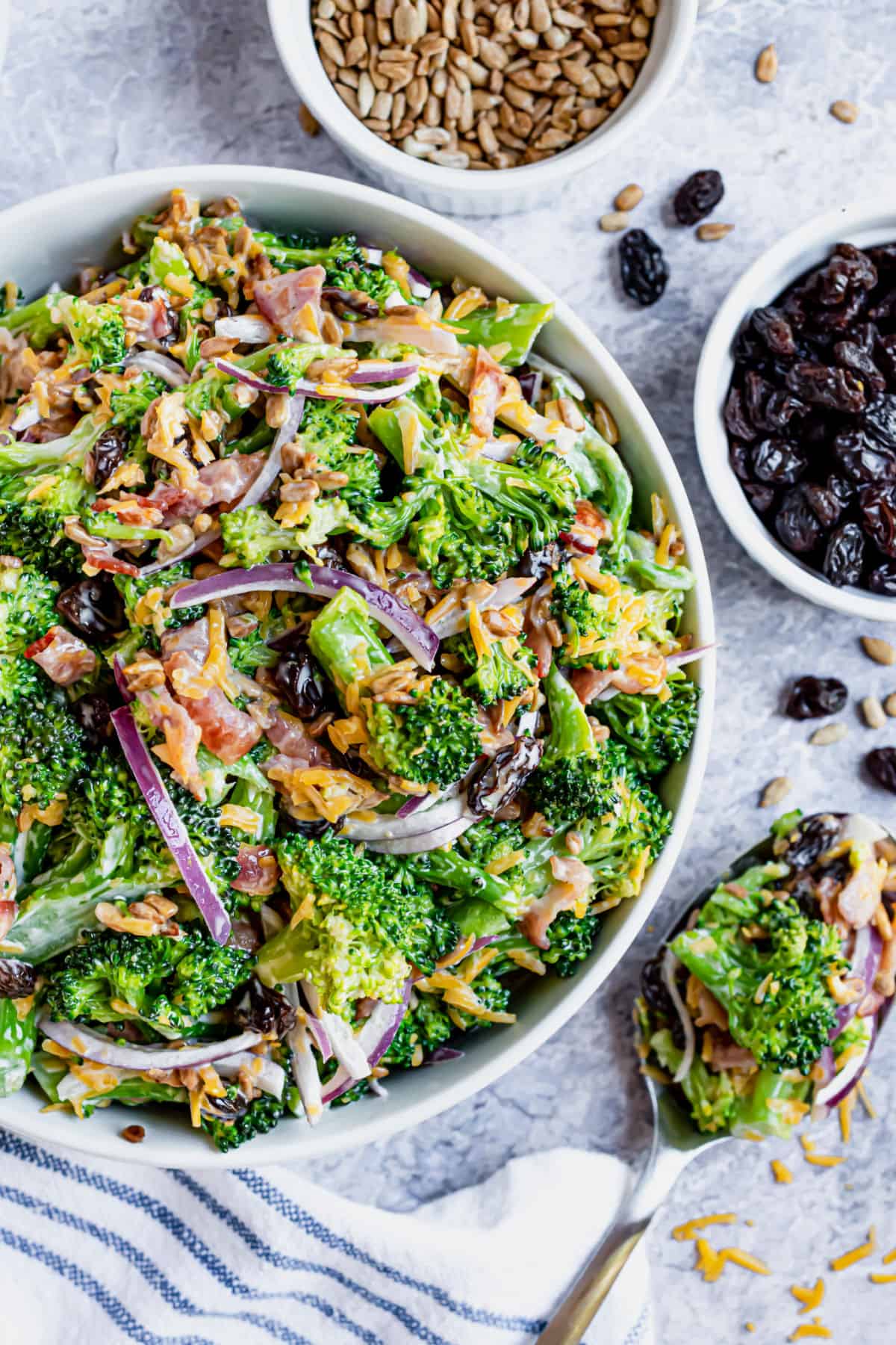 Broccoli salad in serving bowl with side of raisins and sunflower seeds.