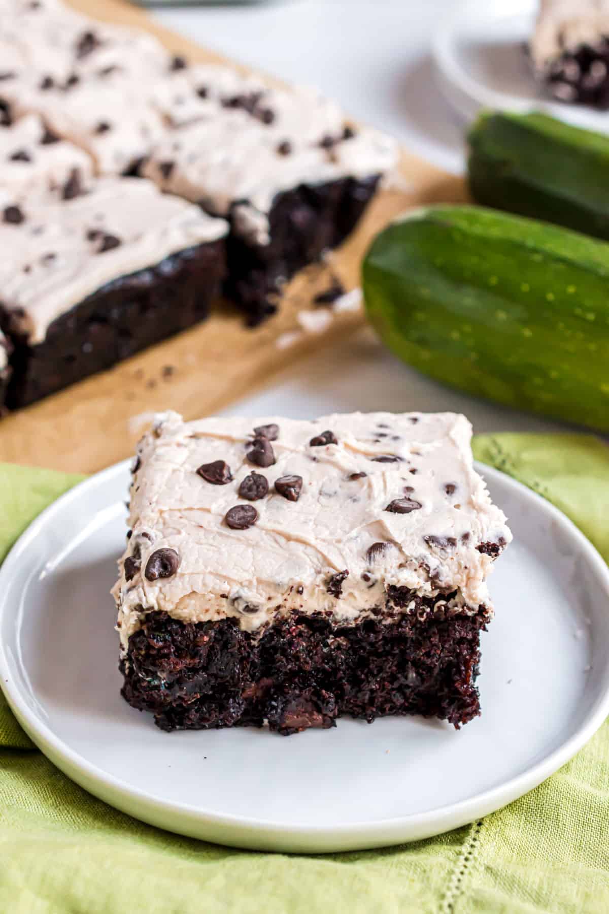 Zucchini brownie on a white plate topped with chocolate chip frosting.