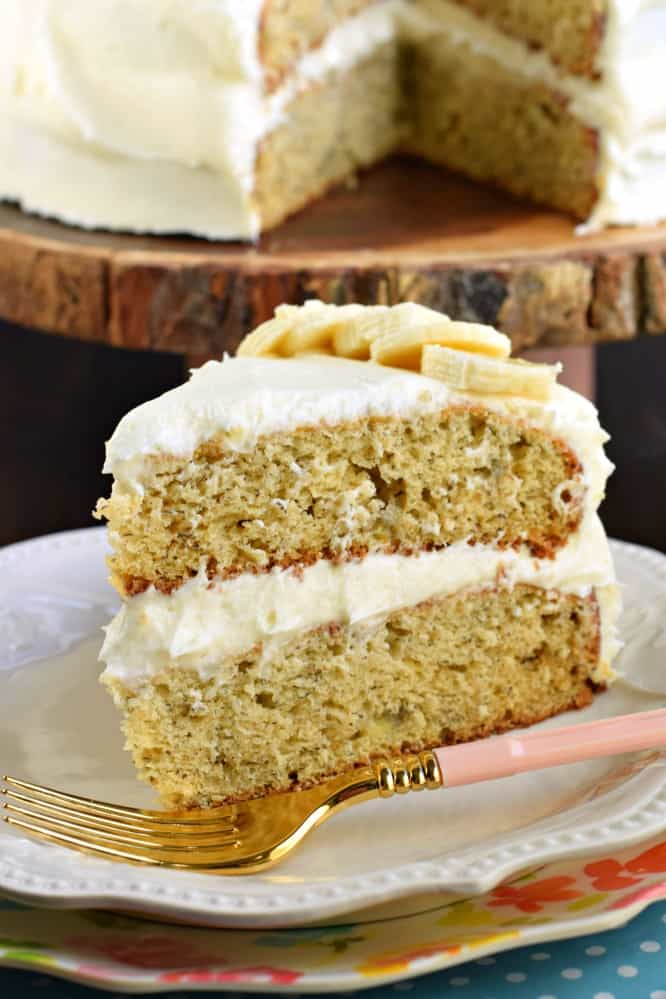 Slice of banana layer cake with cream cheese frosting on a white plate.
