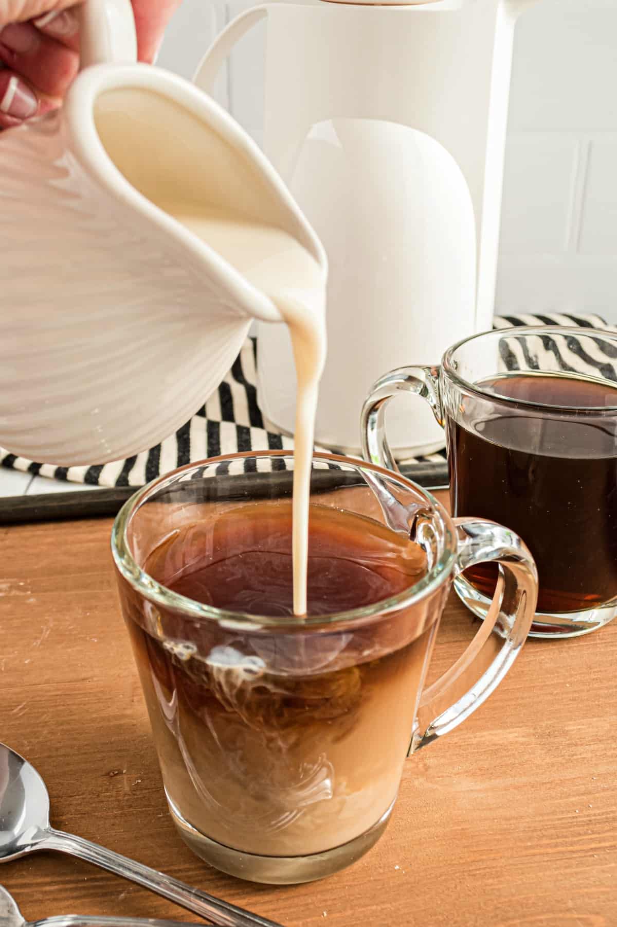 Clear mug of coffee with pitcher of coffee creamer being added to coffee.