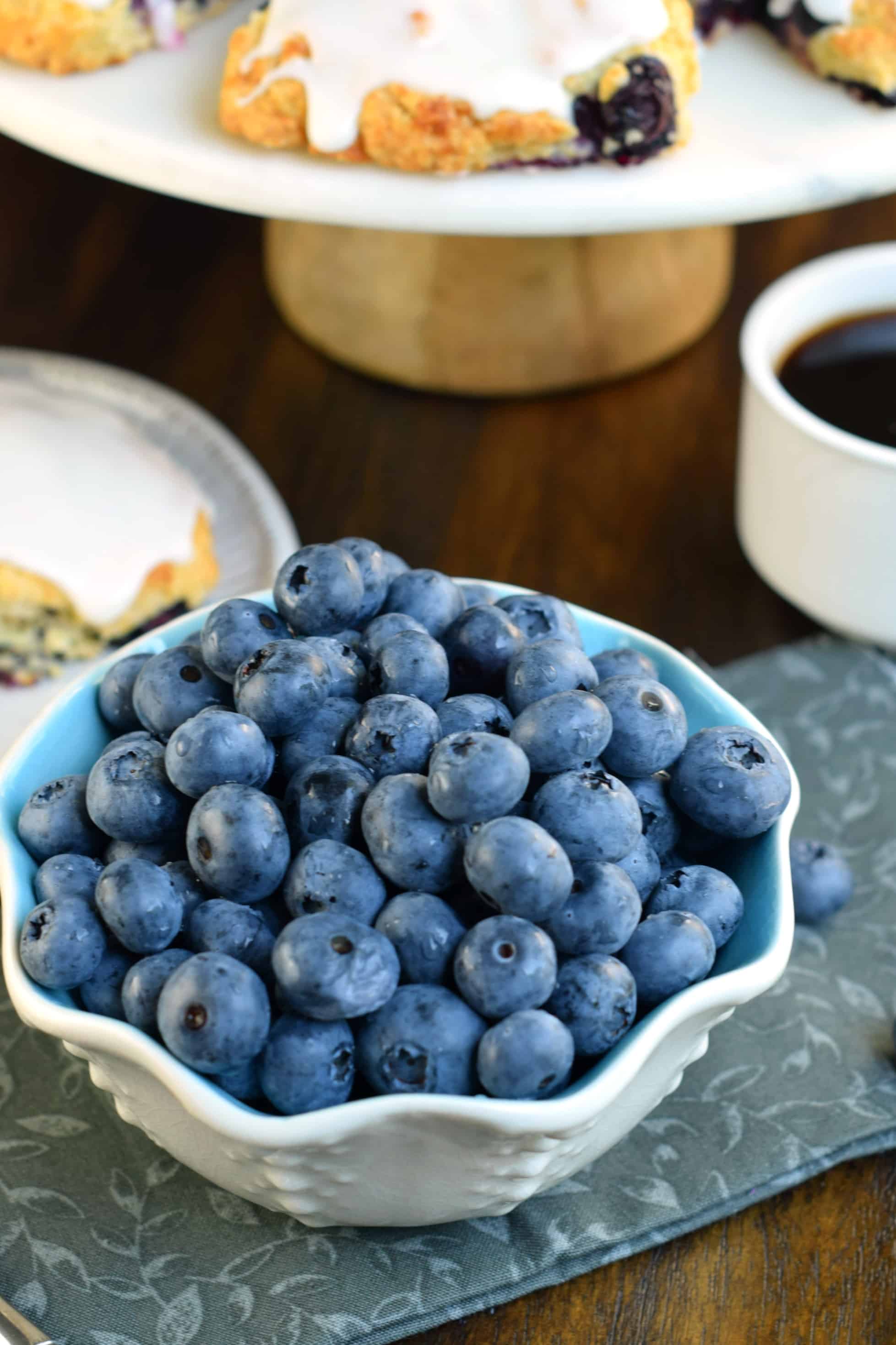 Blueberries in a bowl with a plate of scones in background.