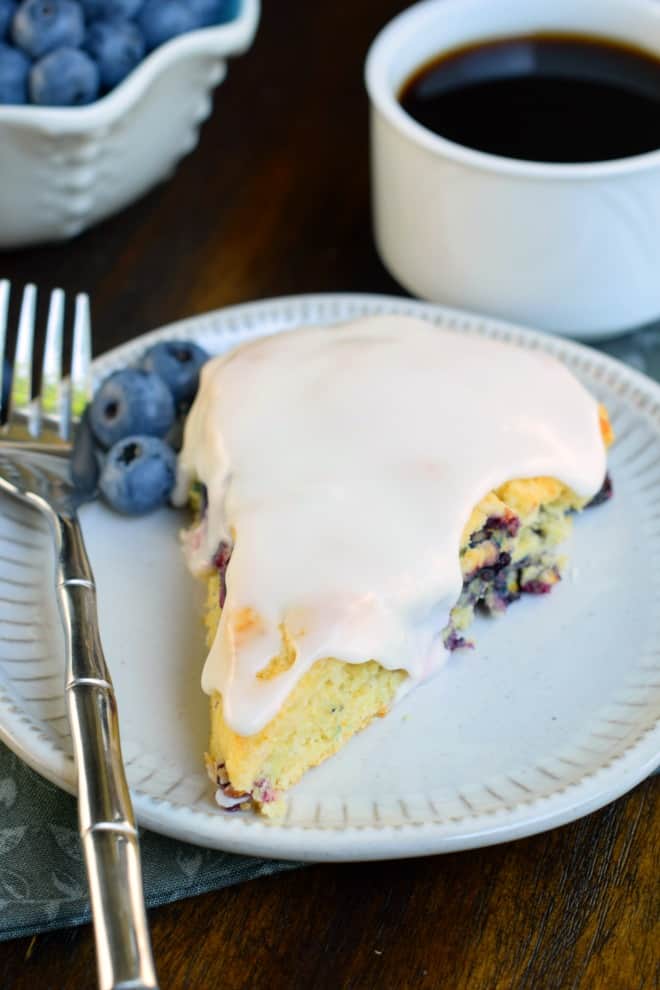 Blueberry scone on a white plate with cup of coffee.